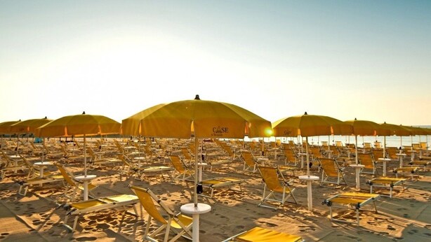 A beach with rows of yellow beach chairs and umbrellas, arranged in a linear pattern along the shoreline. - Agave Apartments (Pisticci)