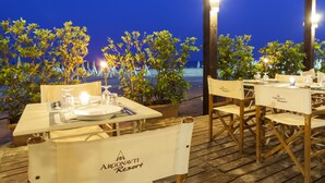 A dining area at Argonauti Resort with tables set for two, potted plants, and a view of the sea. - Agave Apartments (Pisticci)