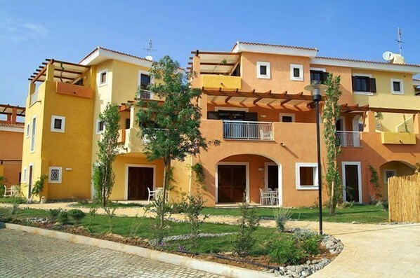 Un edificio residencial con varios balcones, un patio central con mobiliario y un tejado de tejas.