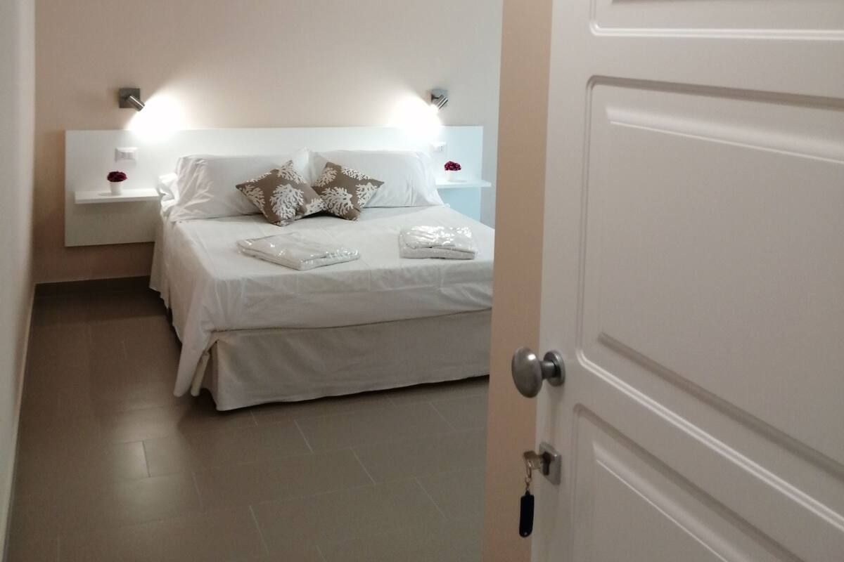 A hotel room with a bed, bedside tables, and a door.