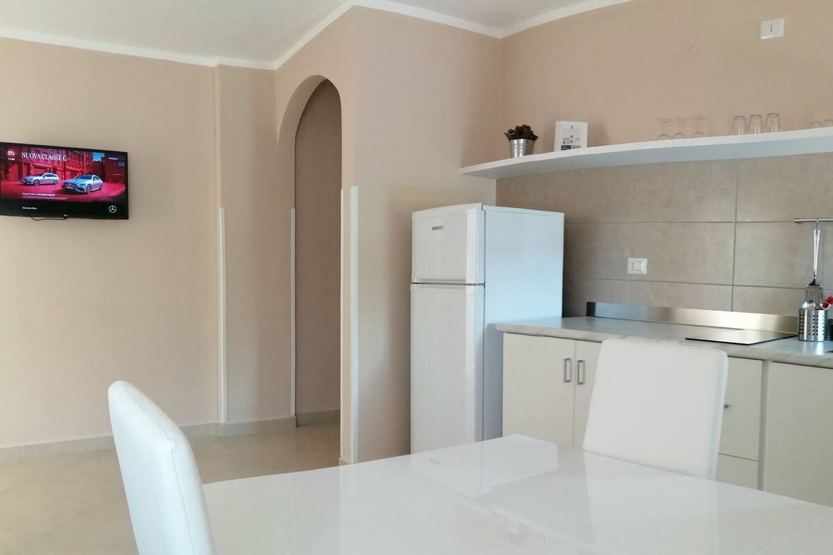 A modern kitchen with a white refrigerator, a built-in oven, a sink with a faucet, and a shelf above the counter.