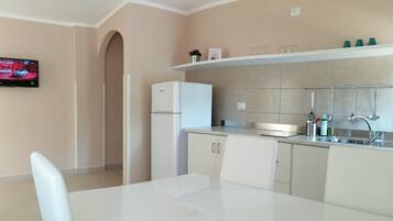 A modern kitchen with a white refrigerator, a built-in oven, a sink with a faucet, and a shelf above the counter.