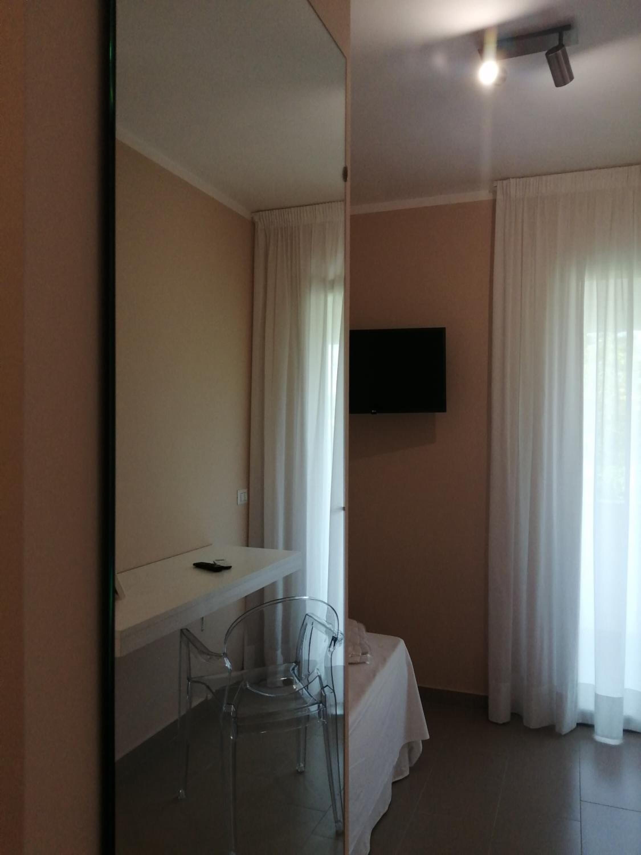 Une chambre d’hôtel équipée d’un lit, d’un bureau, d’une chaise, d’un téléviseur fixé au mur et d’une fenêtre avec des rideaux.