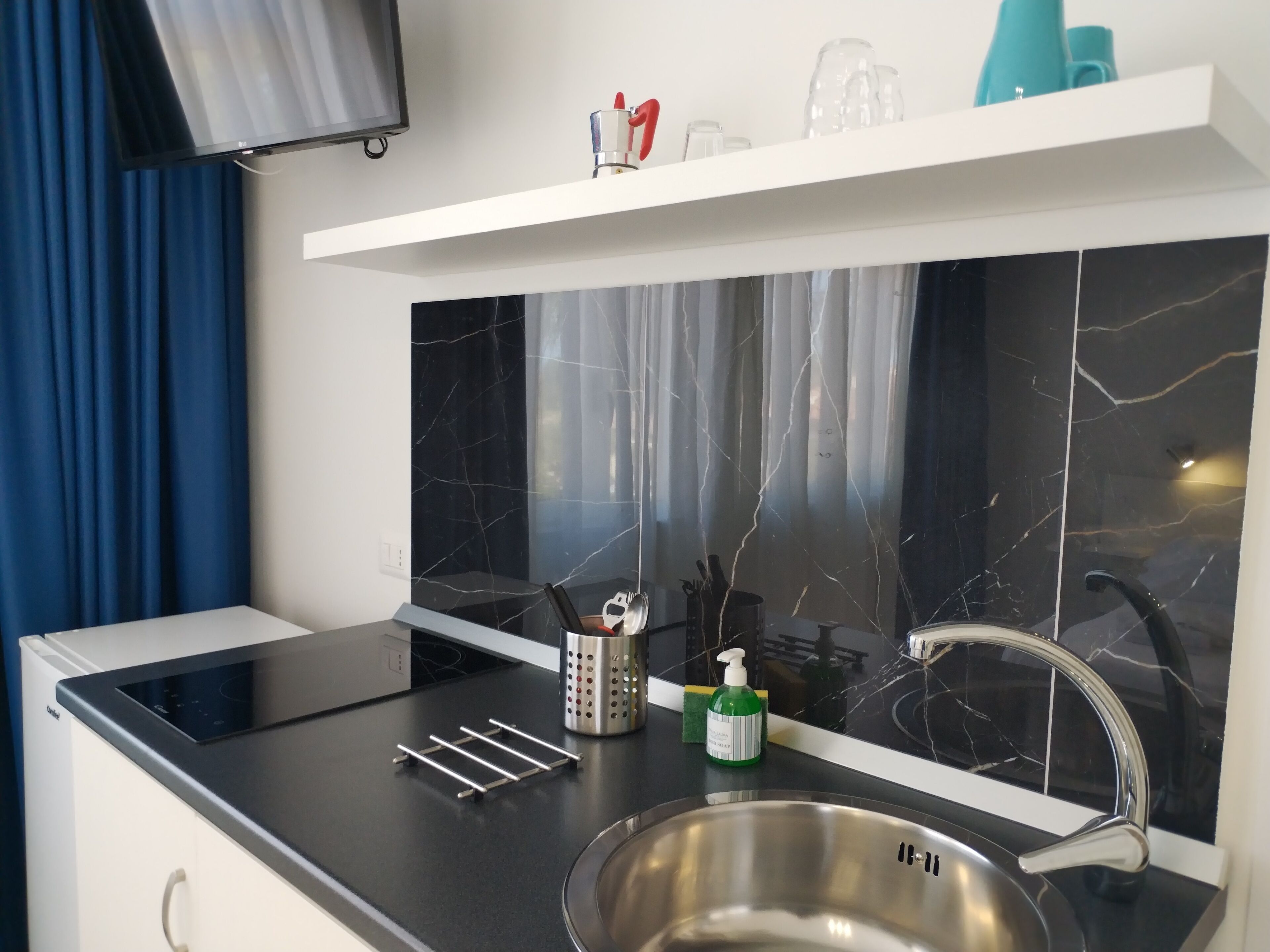 A modern kitchen with a black marble backsplash, stainless steel sink, and a flat-screen TV mounted above the counter.