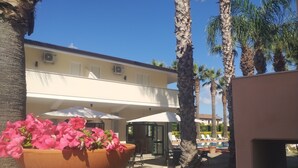 A hotel with a pool area, outdoor seating, and a large flower pot. - Residence Hotel Villa Laura (Ascea)