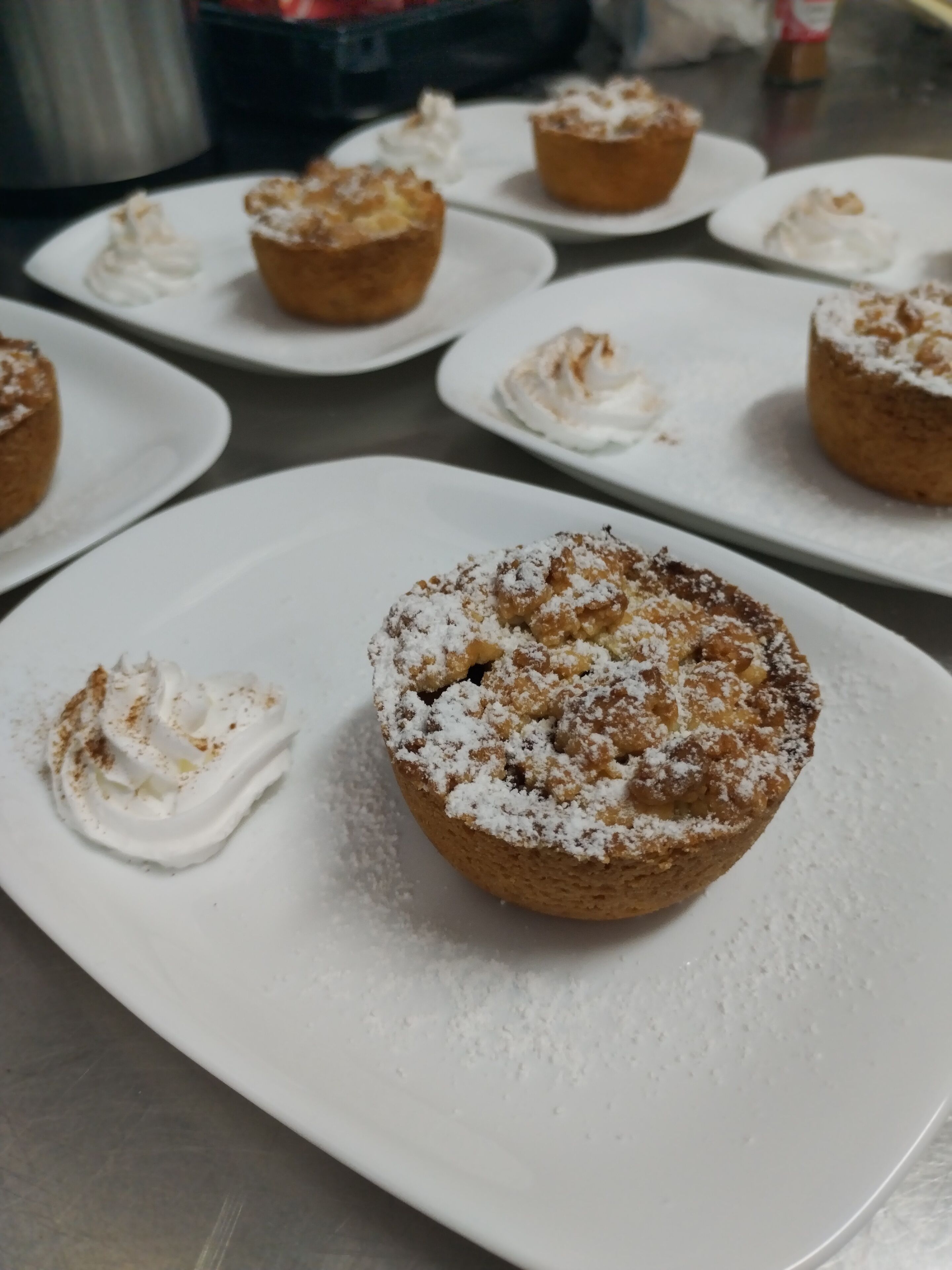 Een tafel met verschillende porties gebak, waaronder een muffin met slagroom en poedersuiker.