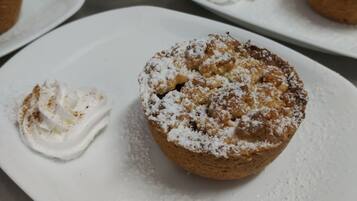 Een tafel met verschillende porties gebak, waaronder een muffin met slagroom en poedersuiker.