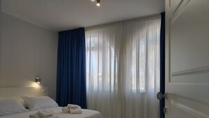 A hotel room with a bed, a nightstand, a wall-mounted lamp, and a window with sheer curtains. - Residence Hotel Villa Laura (Ascea)