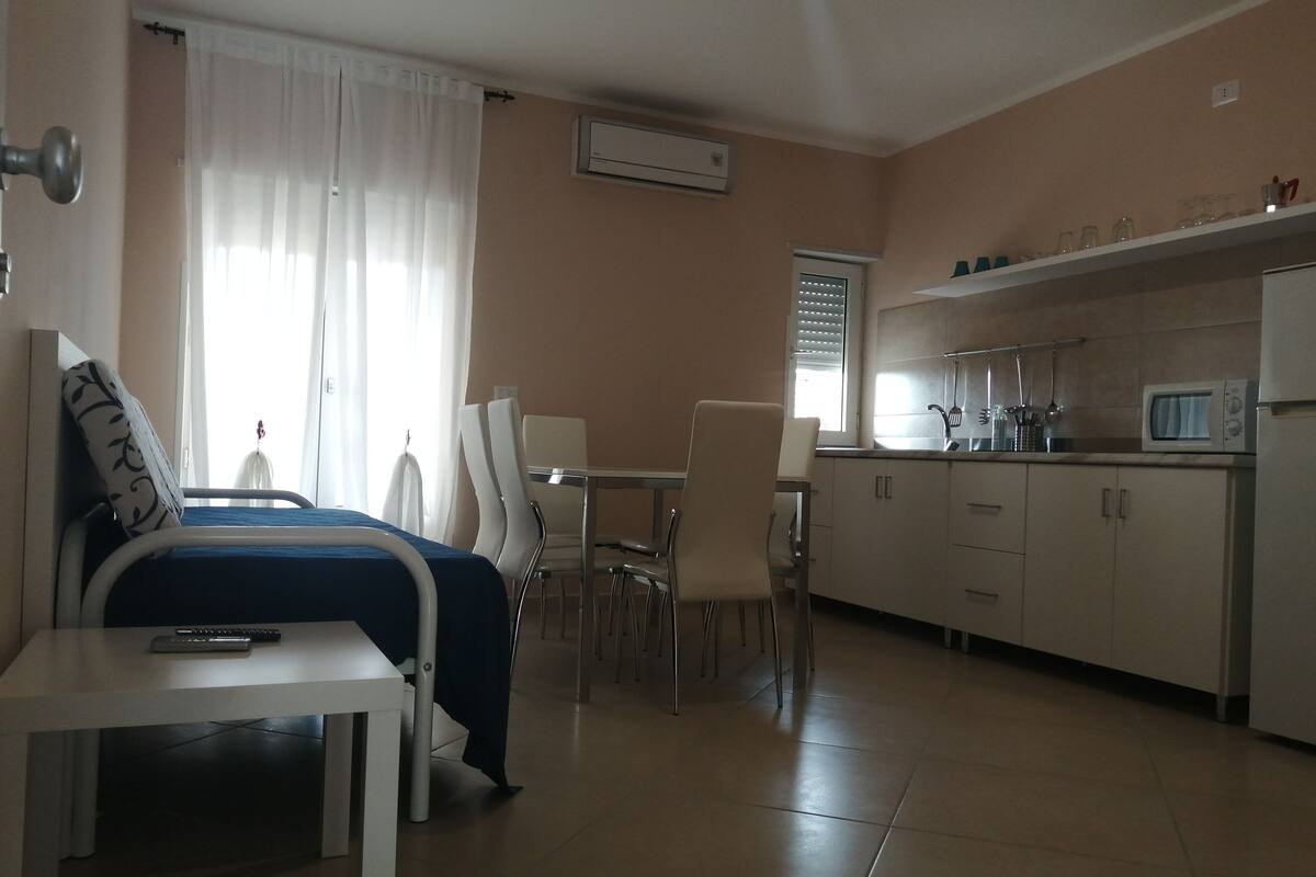 A hotel room with a bed, a desk, a chair, a kitchenette, and a window with curtains.