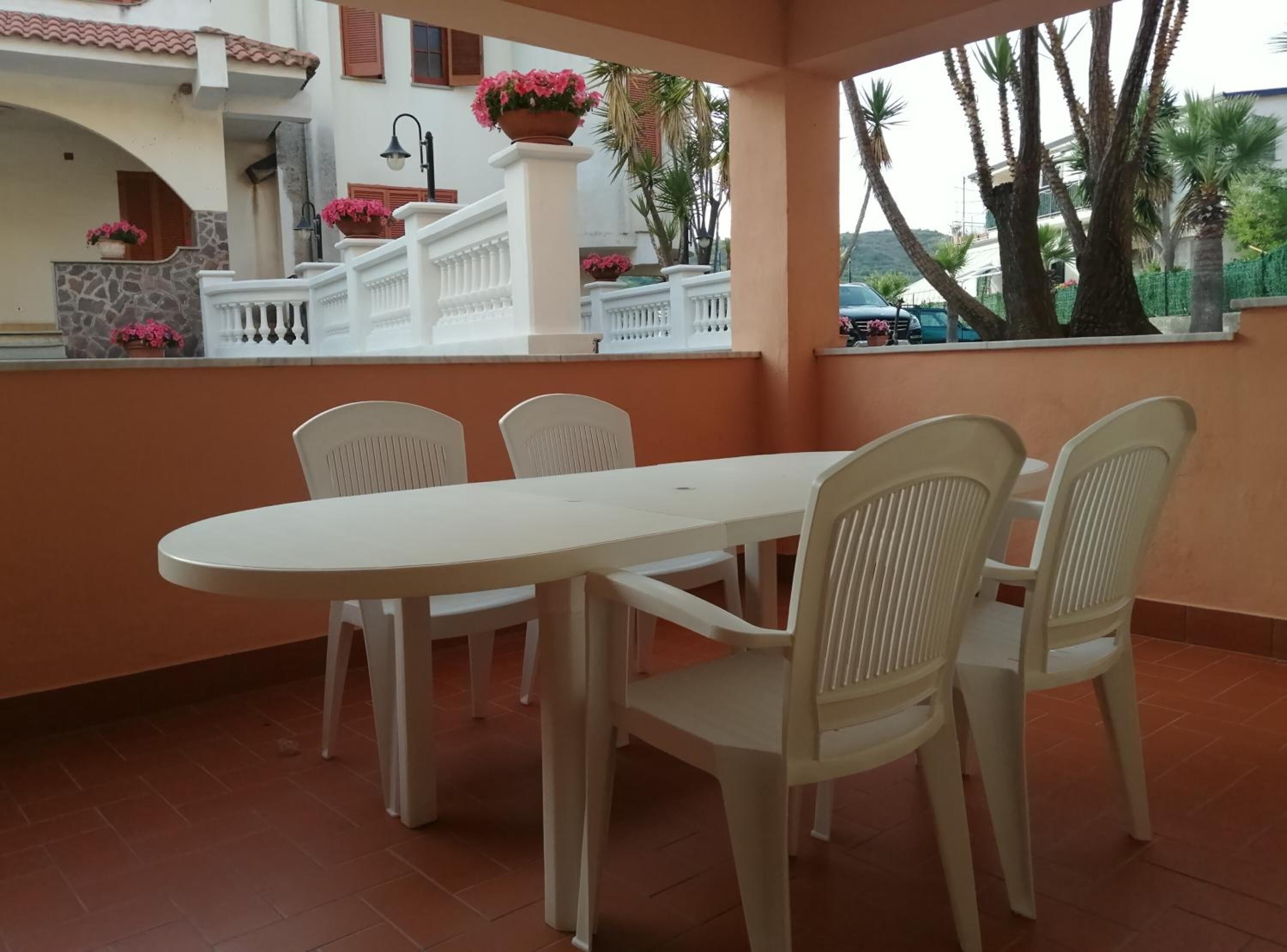 Eine Terrasse im Freien mit einem weißen Tisch und Stühlen, einer Steinmauer und Topfpflanzen.