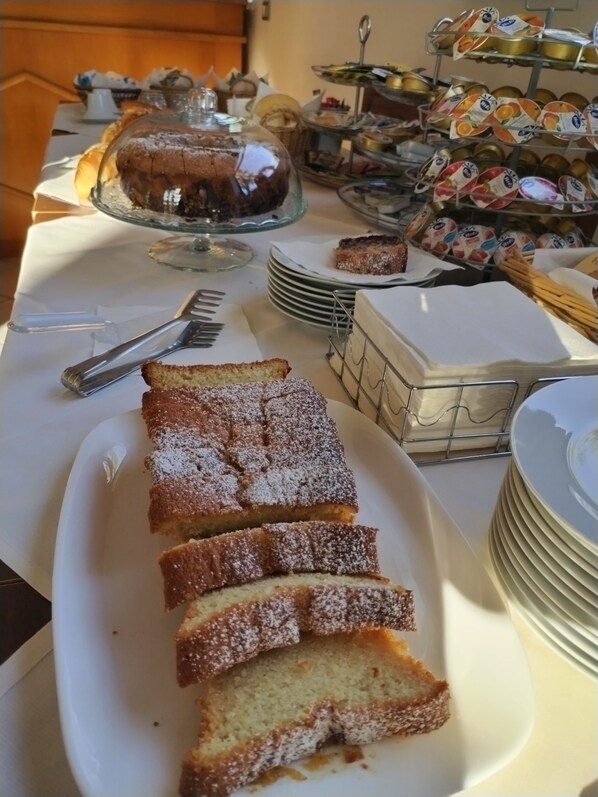 A buffet table with various desserts, including a cake covered with a glass dome, a tray of sliced cake, and multiple containers of yogurt.