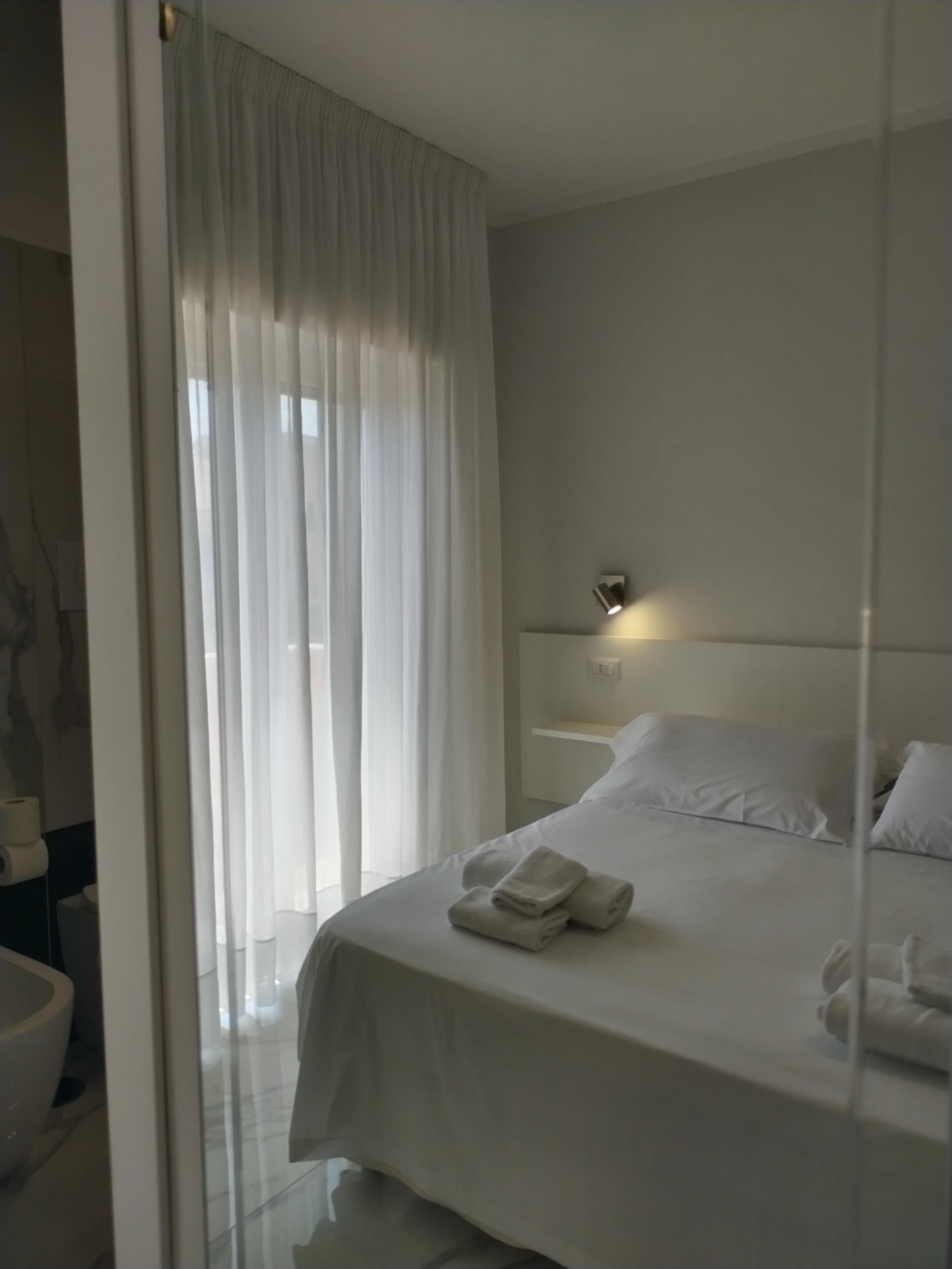A modern hotel room with a large bed, a bedside table, and a bathroom visible through a glass partition.