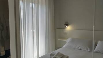A modern hotel room with a large bed, a bedside table, and a bathroom visible through a glass partition.