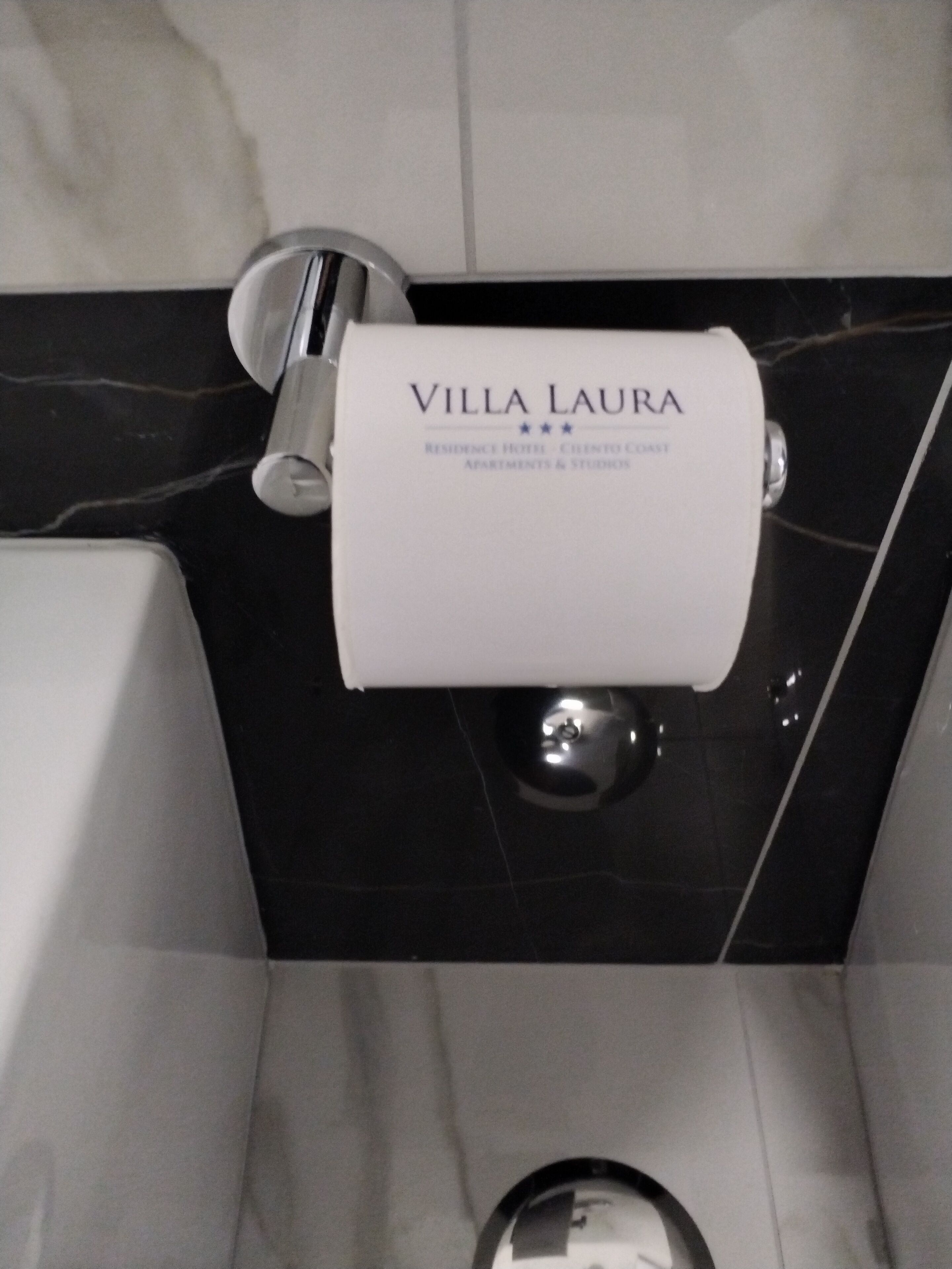 Ein Badezimmer mit Marmorboden, einem weißen Toilettenpapierhalter mit der Aufschrift "VILLA LAURA" und einem chromfarbenen Wasserhahn.