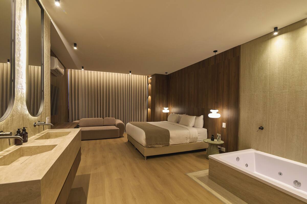 A modern bedroom with a large bed, a separate sofa, a bathtub, and a vanity with a mirror.