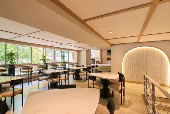 A spacious indoor area with multiple tables and chairs, large windows allowing natural light, and a curved wall with a light fixture. - Hotel Lincoln (MedellĂn)