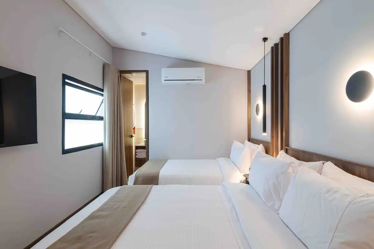 Habitació d'hotel amb dos llits, televisió, aire condicionat i una làmpada de nit.