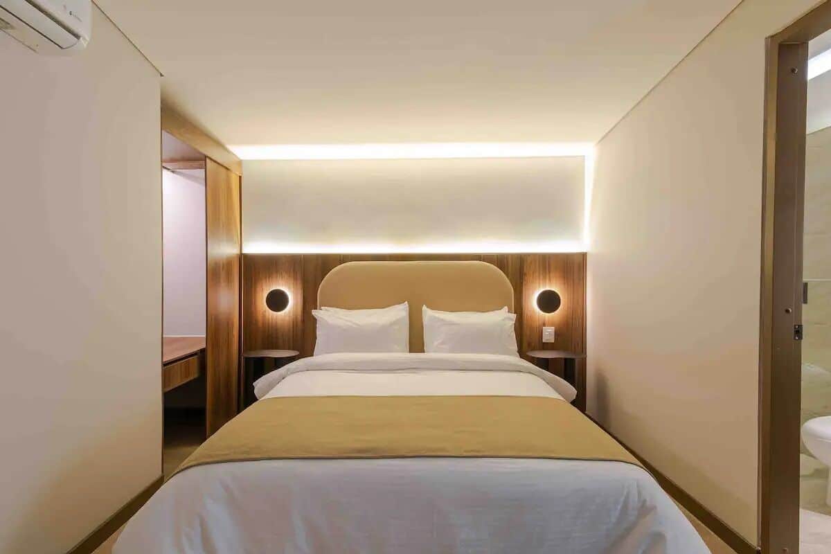 A hotel room with a bed, bedside tables, and a headboard with circular light fixtures.