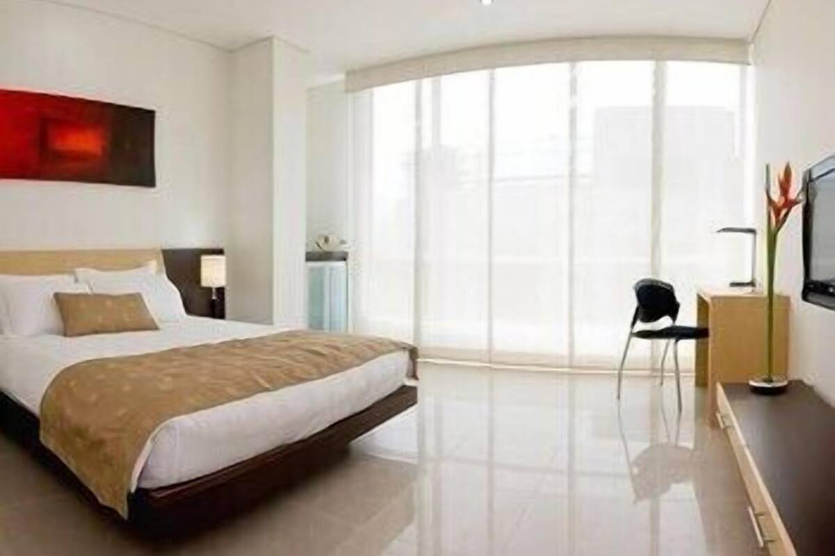 A modern hotel room with a large bed, a desk, a chair, and a TV.