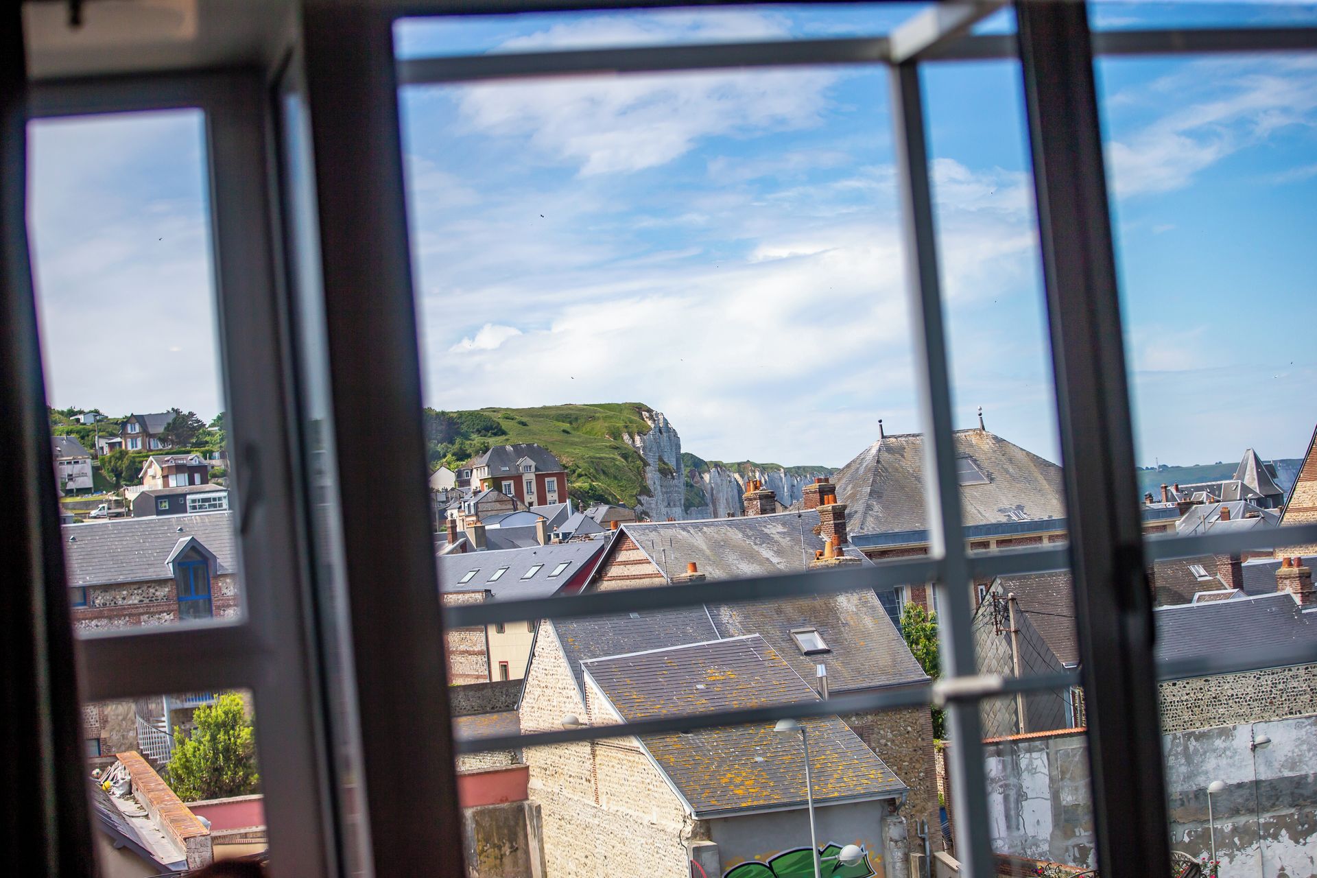 A view through a window of a town with buildings, a hill, and a clear sky.
