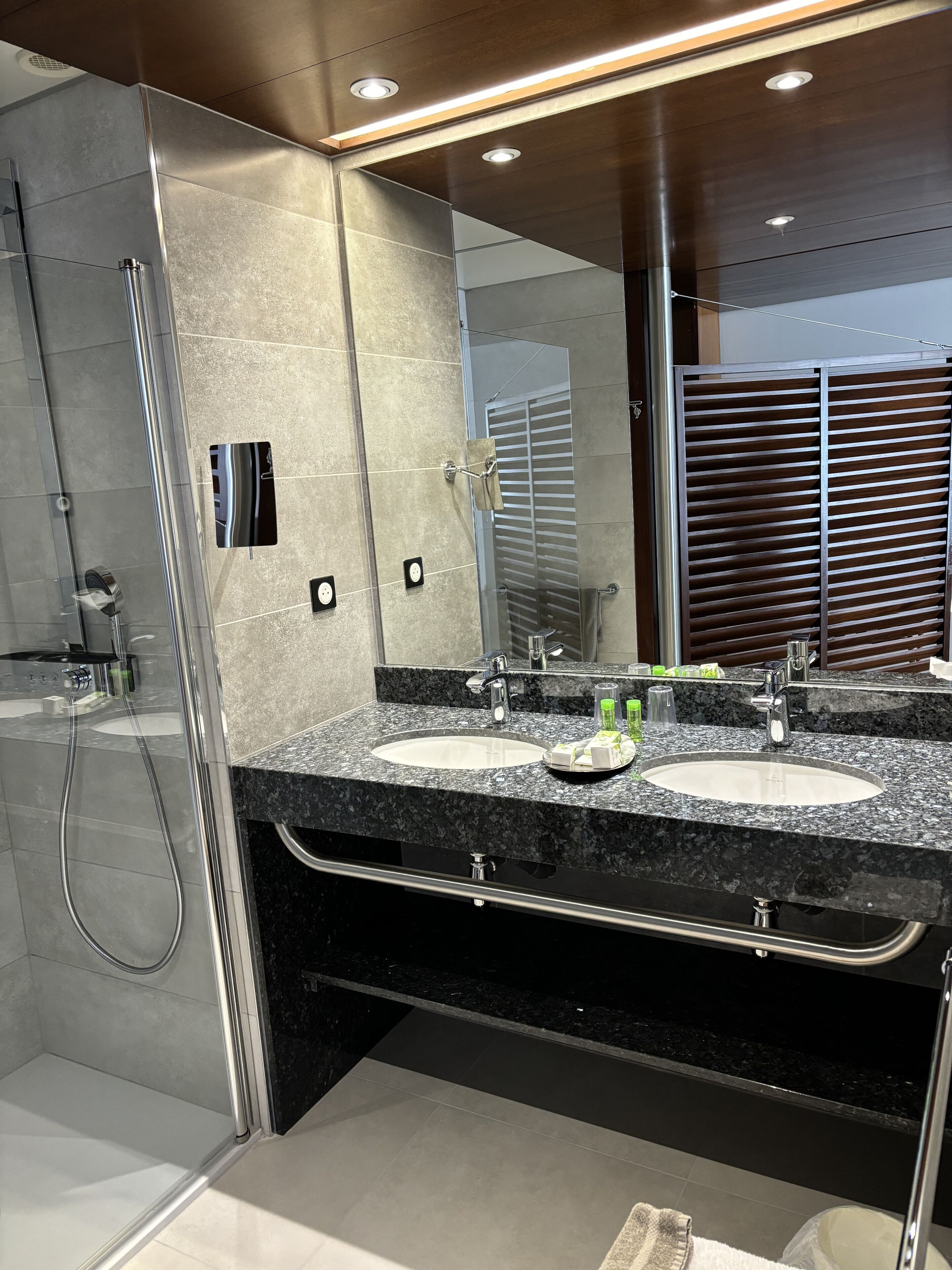 Un baño moderno con ducha envuelta en vidrio, dos lavamanos y un espejo grande.