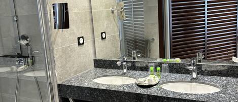 Un baño moderno con ducha envuelta en vidrio, dos lavamanos y un espejo grande.