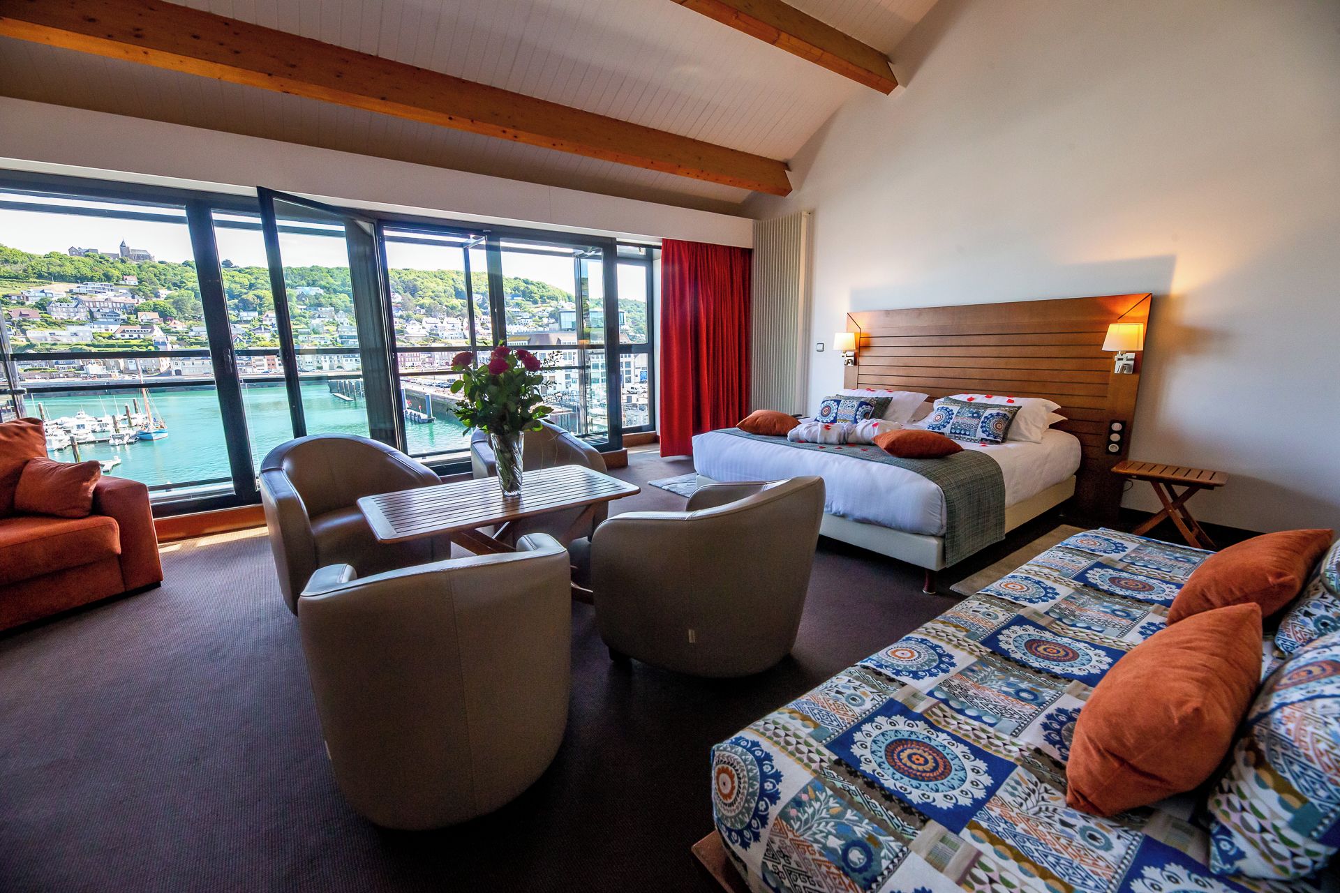 A hotel room with a bed, seating area, and a view of a harbor.