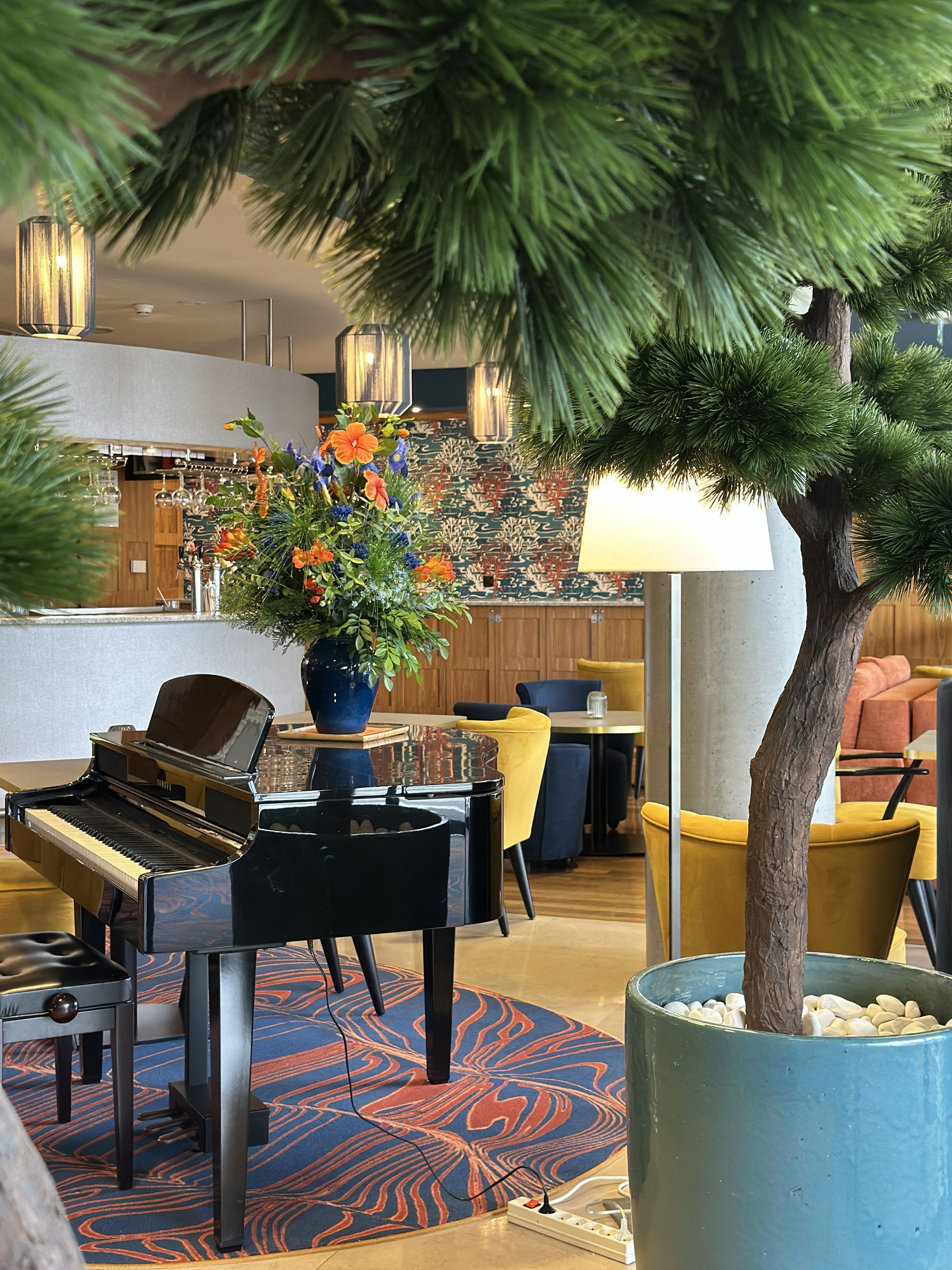 A piano, a dining area, a large potted plant, and a modern lamp.
