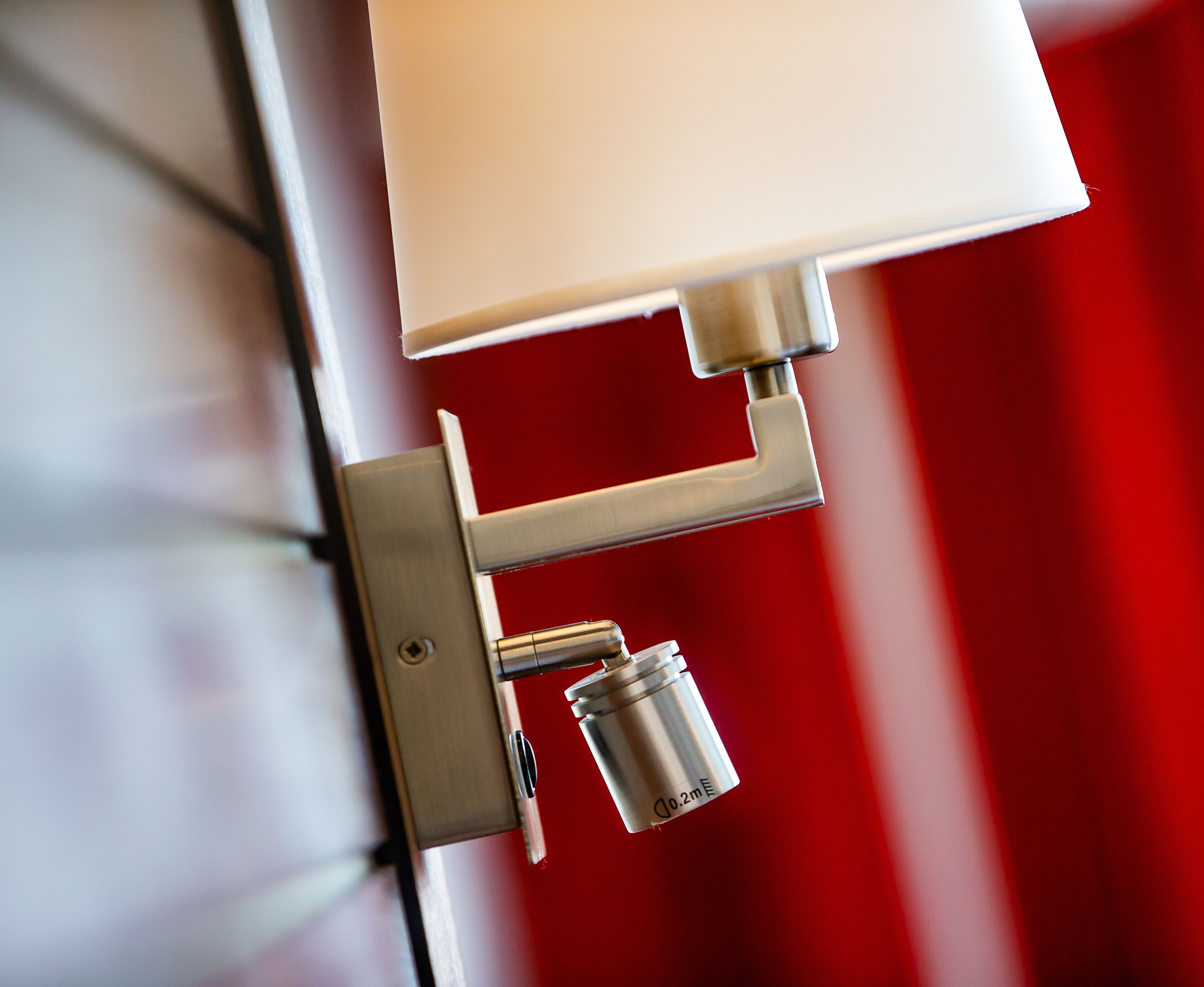 A metallic light fixture with a white lampshade mounted on a wall.