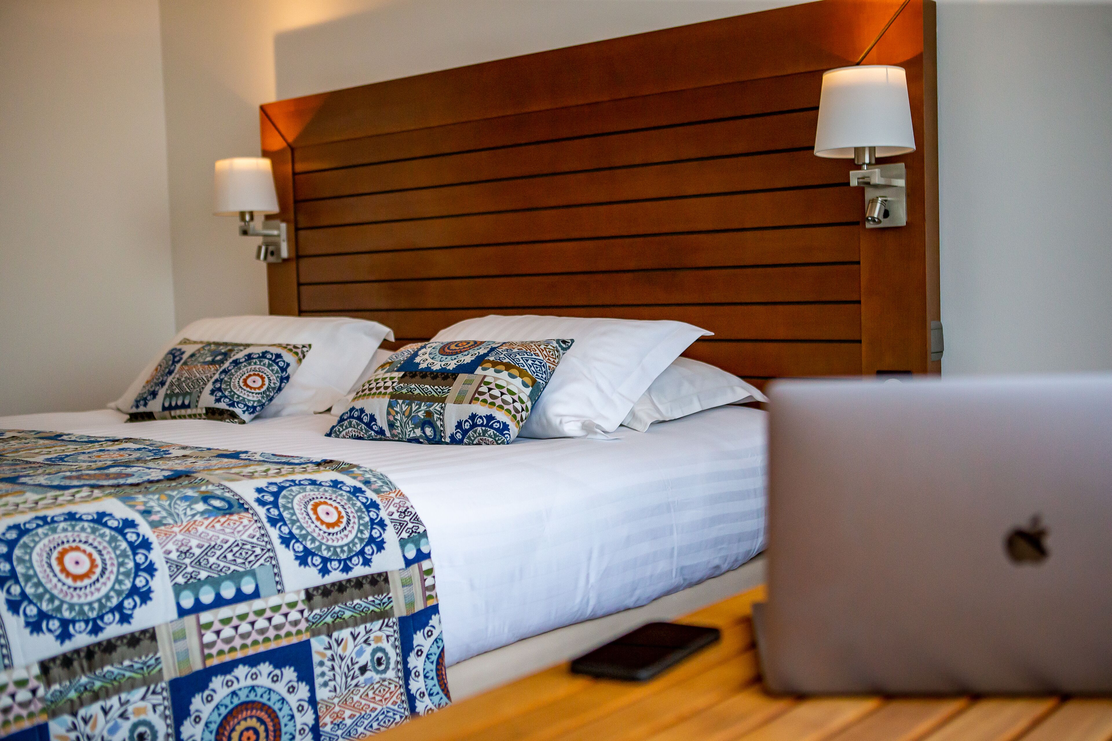 A neatly made bed with patterned bedding, a wooden headboard, and two wall-mounted lamps.