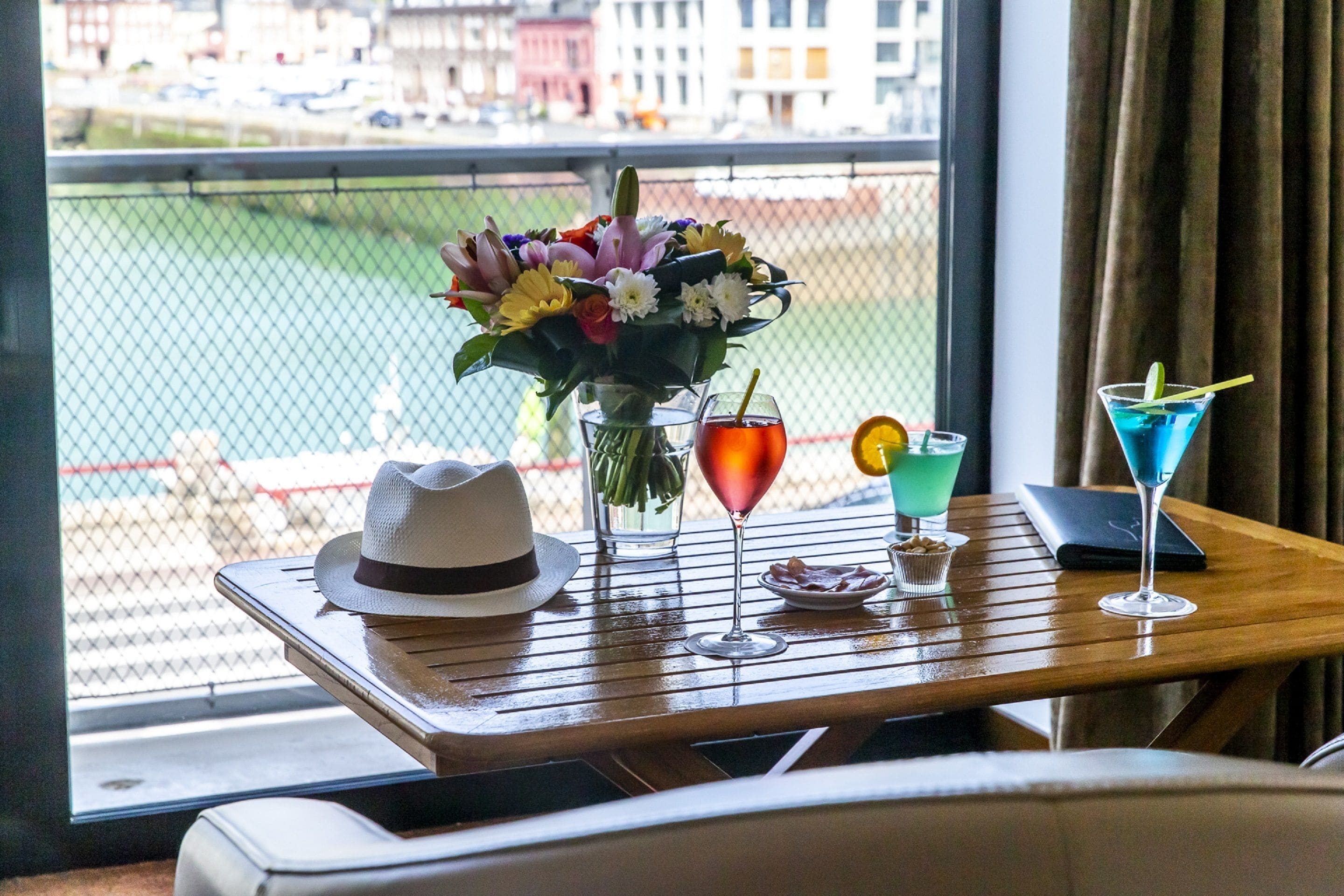 Ein Tisch mit einem weißen Hut, einer Blumenvase und drei Getränken.