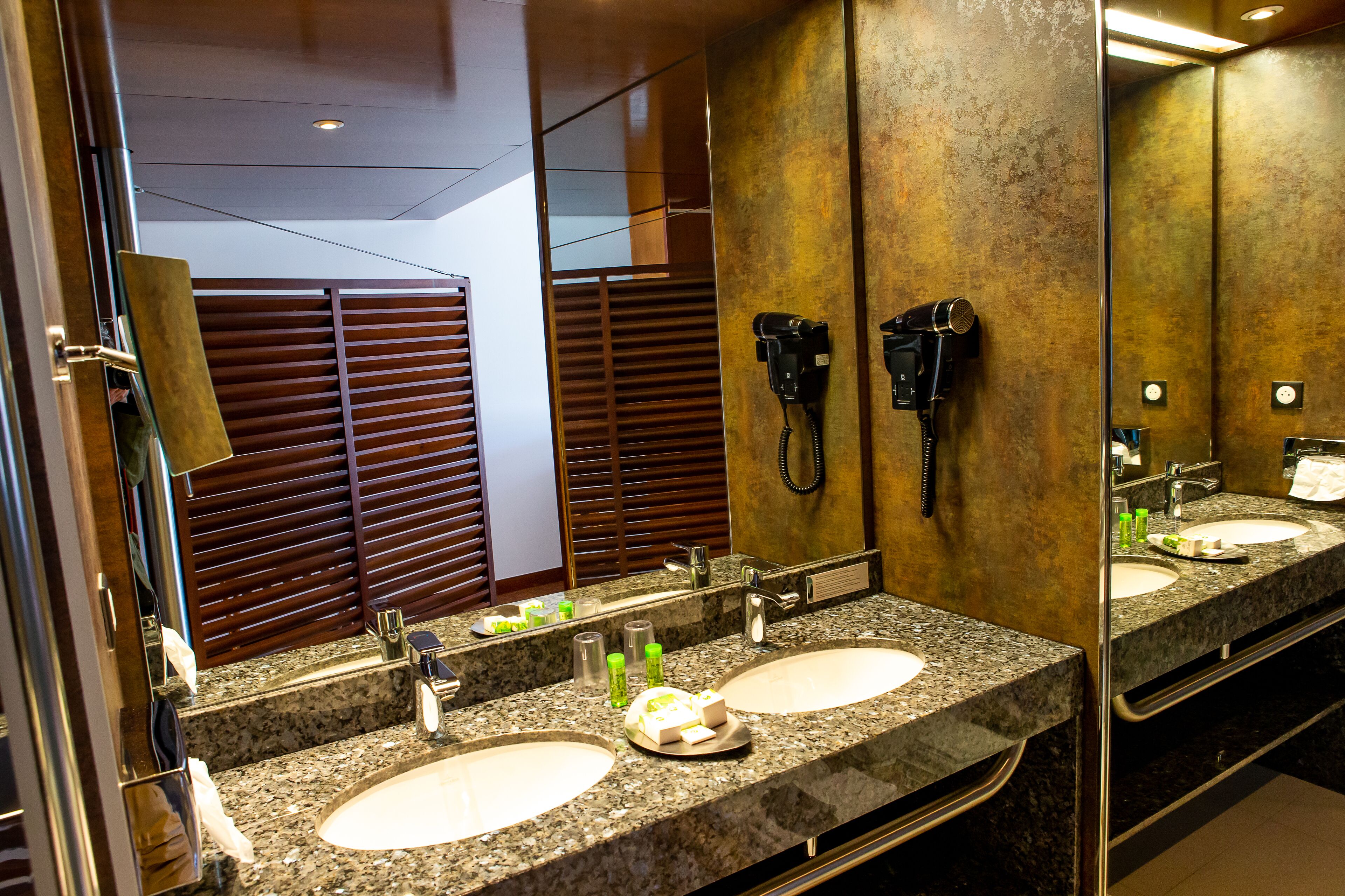 A hotel bathroom with two sinks, a hairdryer, and a mirror.