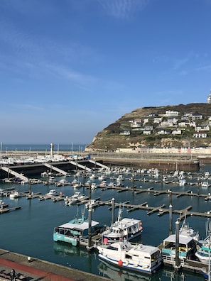 A marina with boats docked, a lighthouse in the background, and a hillside with buildings. - Le Grand Pavois (Fecamp)