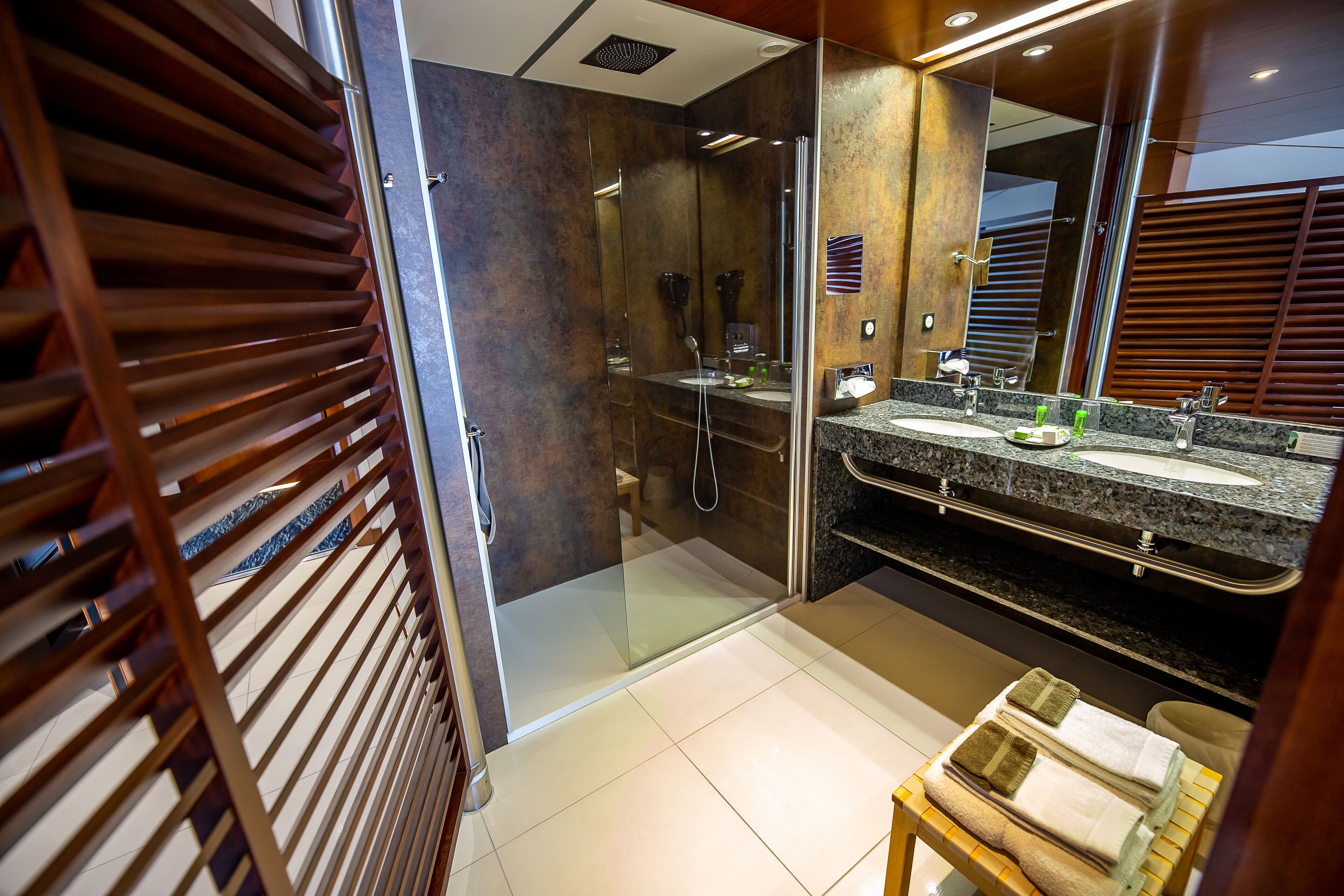 Un baño moderno con ducha de vidrio, lavabo de encimera de granito y un espejo grande.