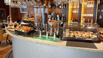 A buffet bar with various food items, a selection of wine glasses, and a variety of bottles.