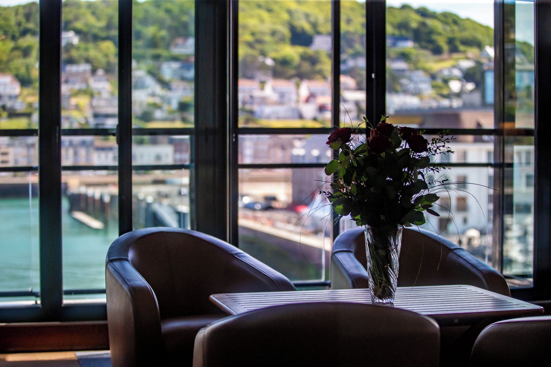 A view from a window with a table and chairs, a vase with flowers, and a cityscape in the background.