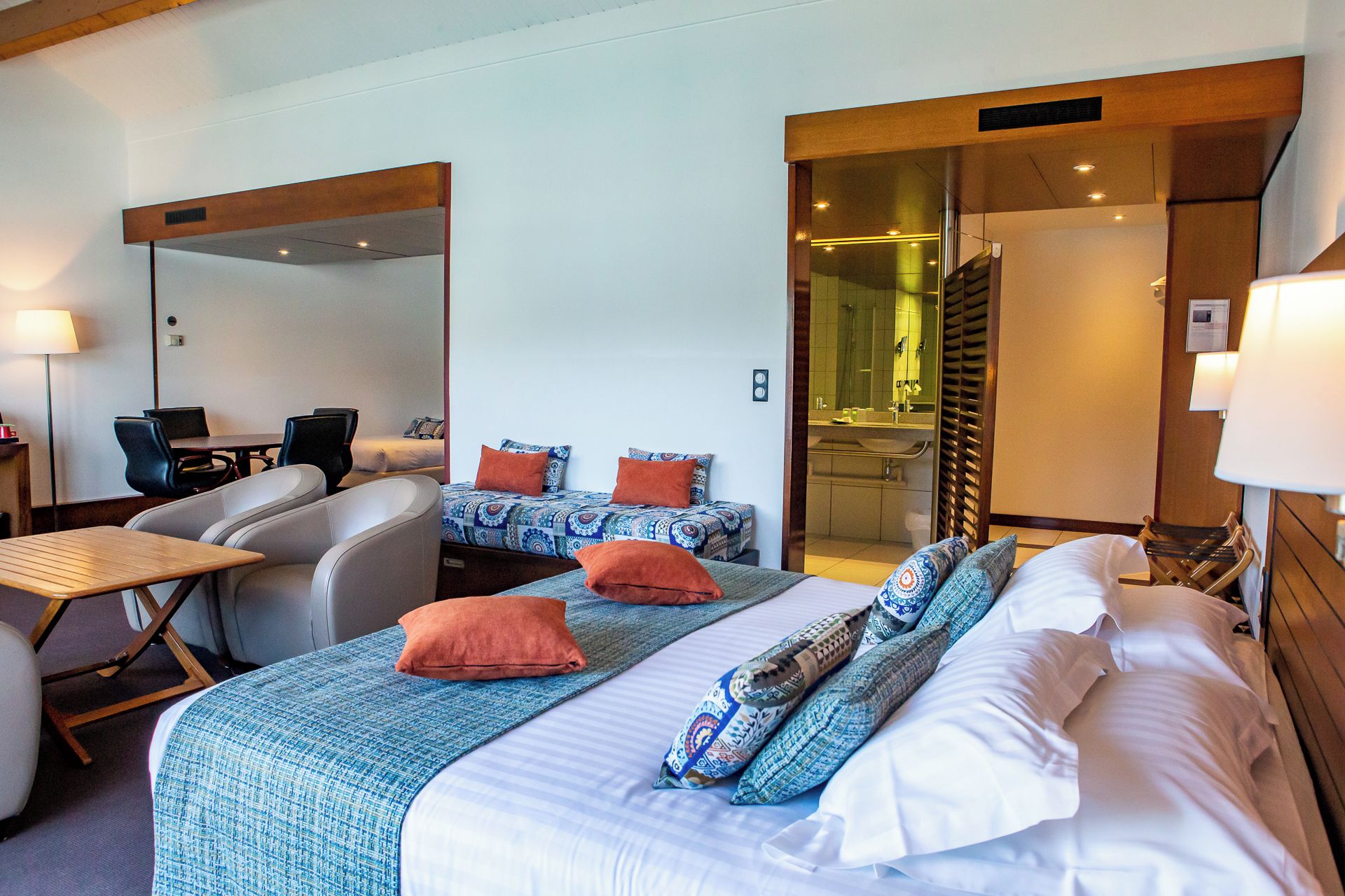A hotel room with a bed, a desk, a chair, a mirror, and a bathroom visible through a glass door.