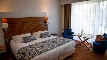Ein Hotelzimmer mit einem großen Bett, einem Schreibtisch mit Laptop, zwei Stühlen und einem Fenster mit Vorhängen.
