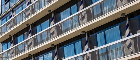 Un edificio de varios pisos con un diseño arquitectónico moderno, que cuenta con una serie de balcones con barandillas de malla y una vista despejada del cielo a través de las ventanas.