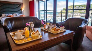 A breakfast setup with a tray of food, a cup, and a glass of orange juice on a wooden table in a room with a view of a marina. - Le Grand Pavois (Fecamp)