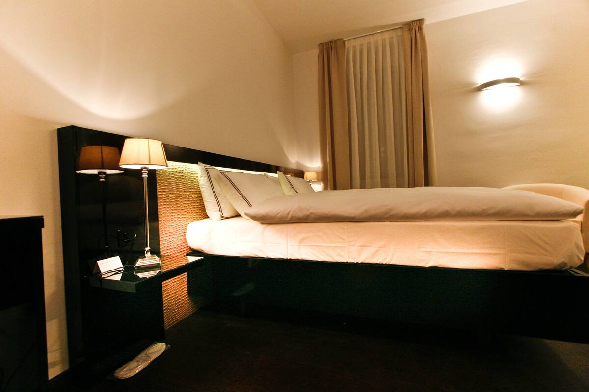 A hotel room with a bed, a nightstand with a lamp, and a wall-mounted light.