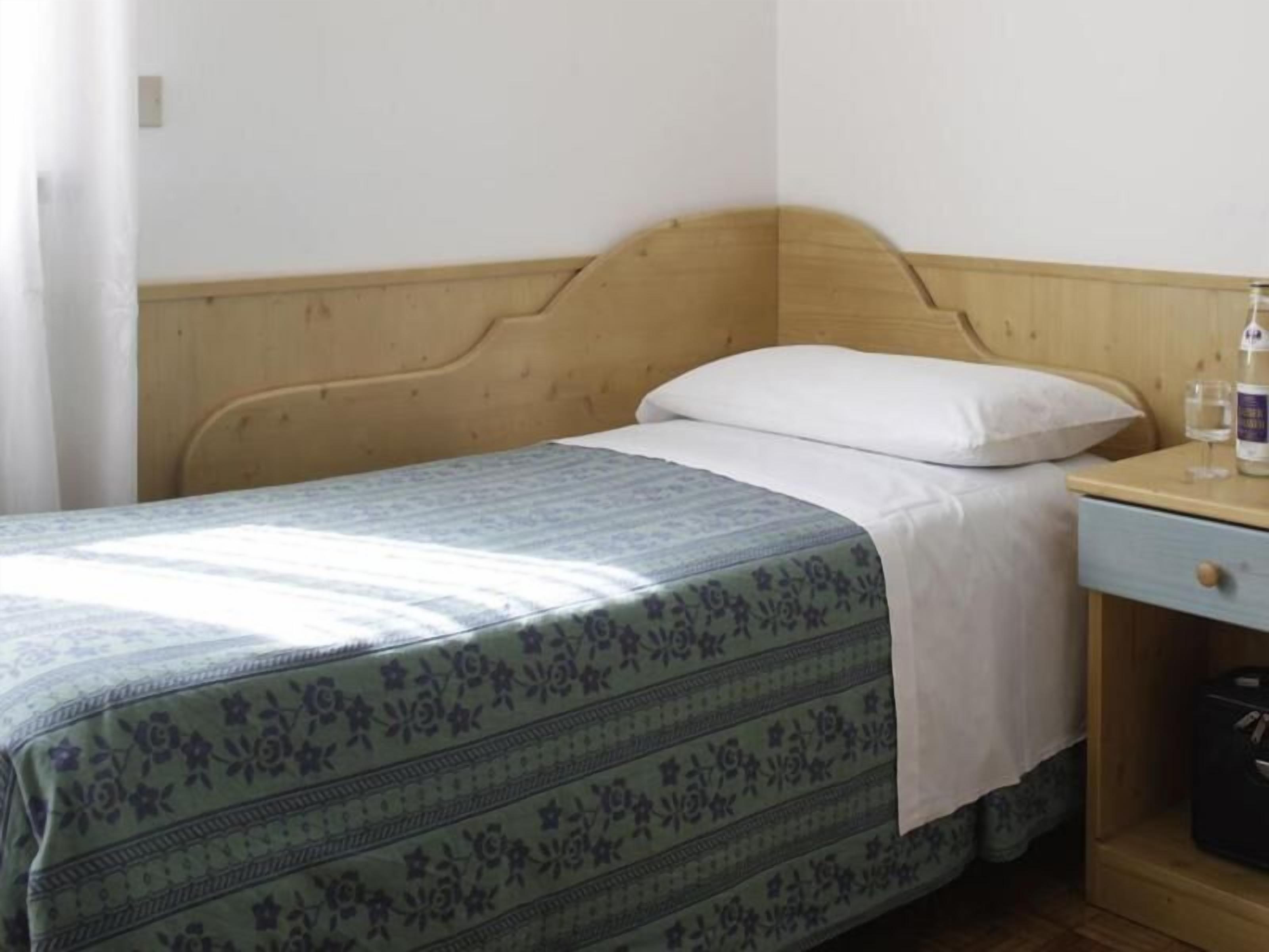 A single bed with a wooden headboard, a bedside table with a drawer, and a bottle of water on the table.