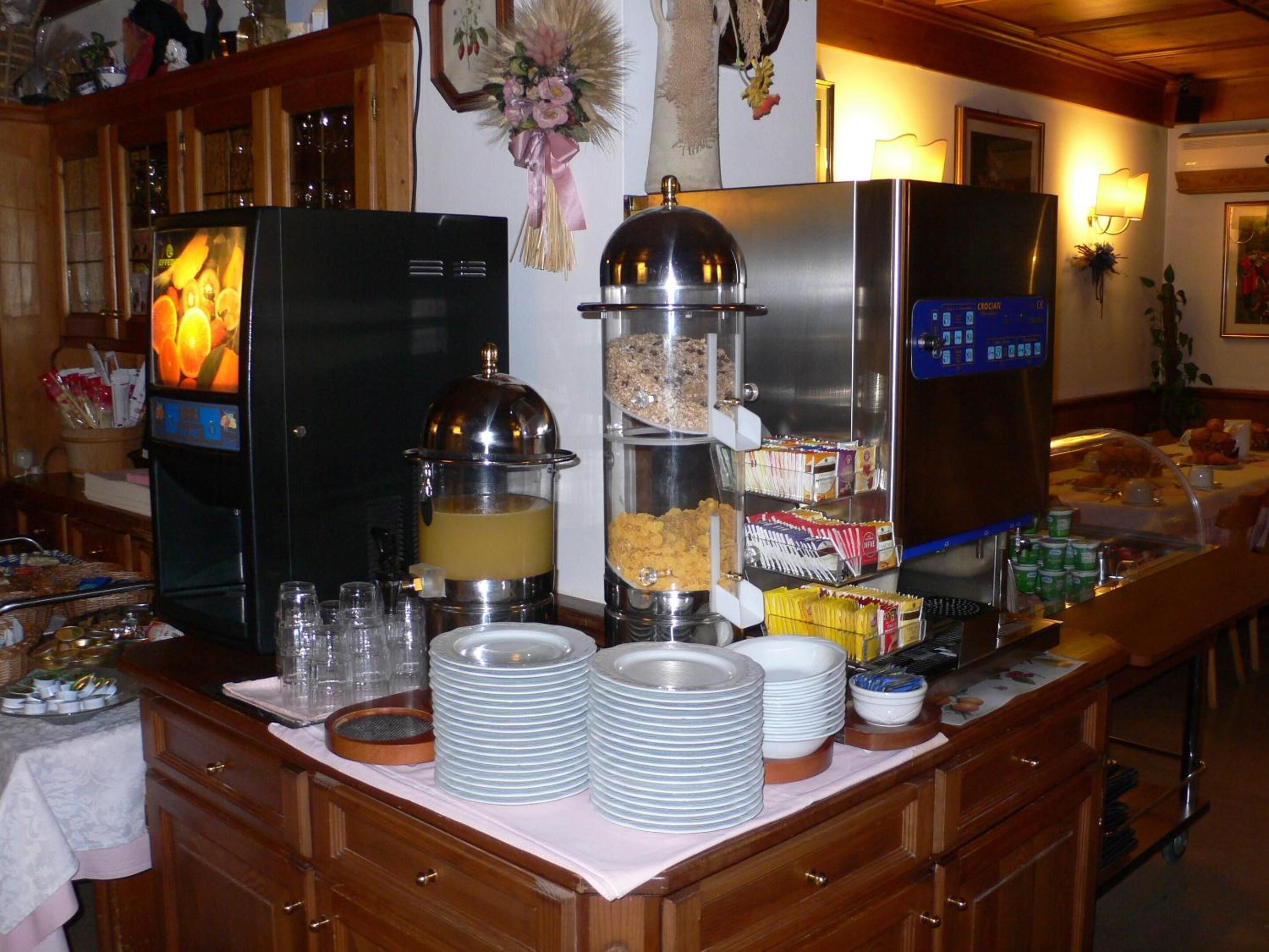 Disposição de buffet com máquina de café, dispensador de suco e diversos alimentos.