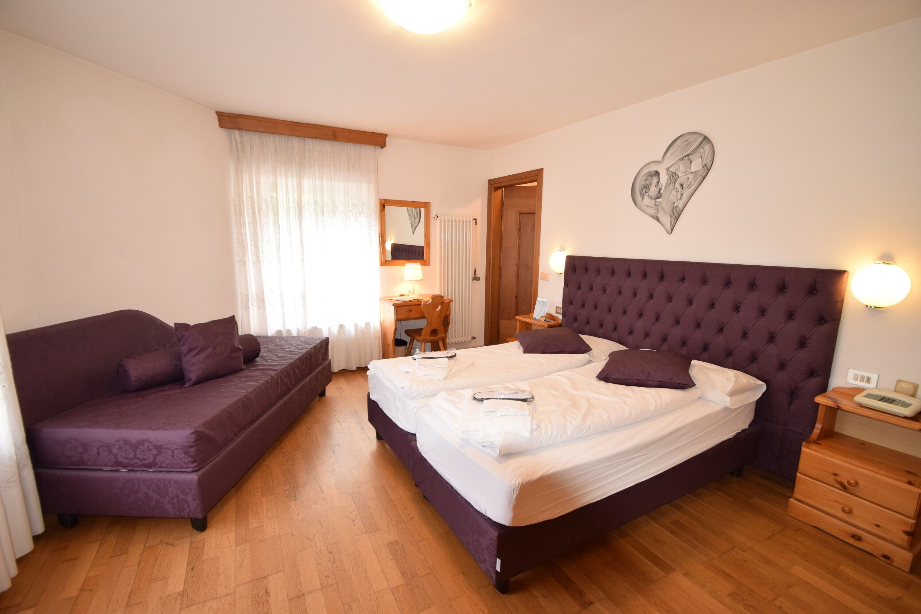 Een slaapkamer met een tweepersoonsbed, een slaapbank, een houten nachtkastje en een wandlamp.