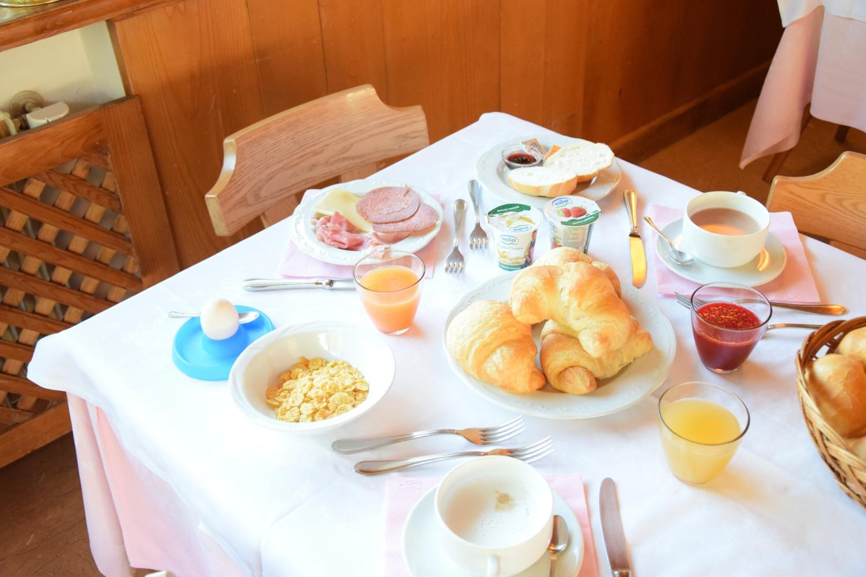 A breakfast table with croissants, eggs, ham, and juice.