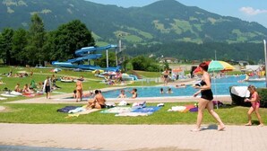 A pool area with a water slide and people sunbathing. - Hubertus (Fuegenberg)