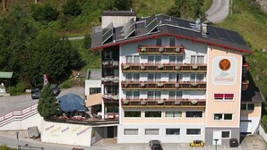 A multi-story hotel with balconies, a parking area, and a road nearby. - Hubertus (Fuegenberg)