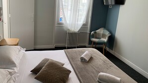 A hotel room with a bed, pillows, a chair, a TV, and a window with curtains. - Hôtel L'ESTRAN (Trouville-sur-Mer)