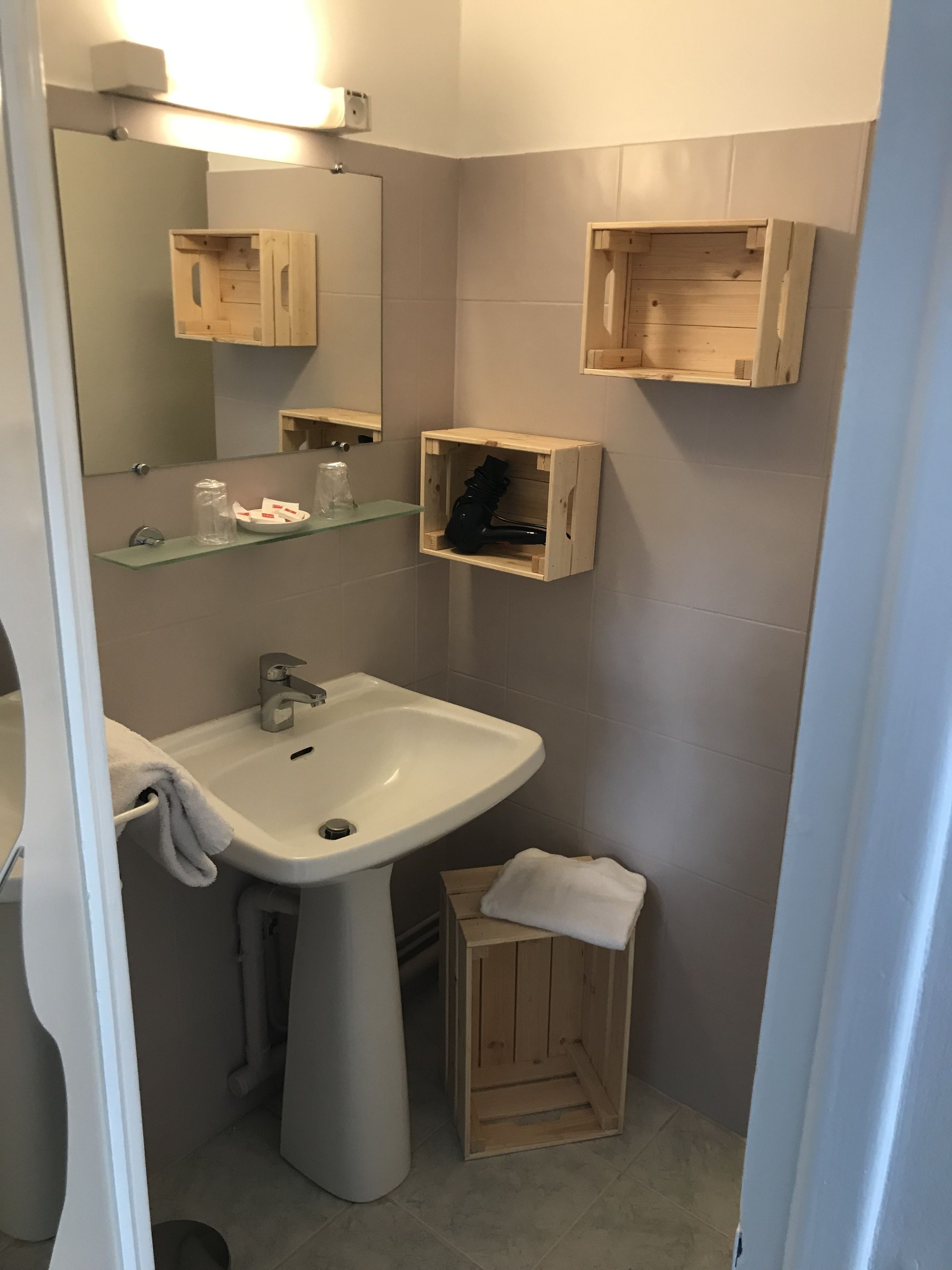 Une salle de bain avec un lavabo sur colonne, un miroir et des boîtes de rangement en bois.