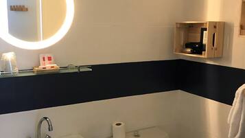 A bathroom with a sink, toilet, and a mirror with a light. There is a small wooden cabinet with toiletries.